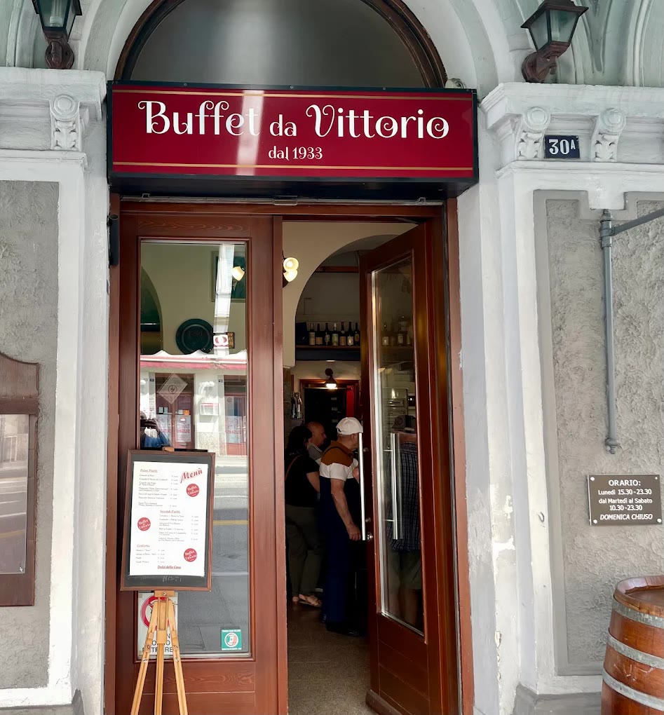 L'ingresso del Buffet da Vittorio al civico 30/A di via Carducci: porta in legno e vetro sotto l'insegna rossa «Buffet da Vittorio dal 1933», con la targa degli orari e il menu su un cavalletto